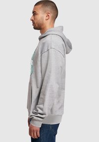 Gray hoodie with a front pouch pocket, ribbed cuffs and hem, featuring a graphic print. Fabric appears soft and textured.