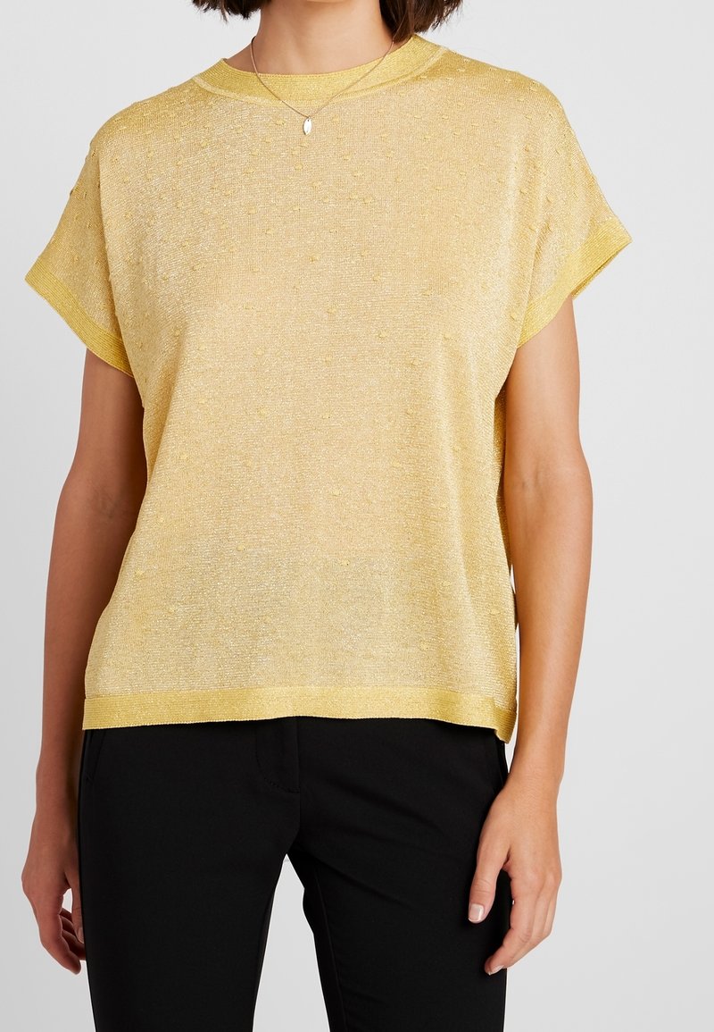 Haut jaune à manches courtes avec une finition texturée. Le tissu a un effet scintillant avec de petits points en relief et une coupe décontractée.