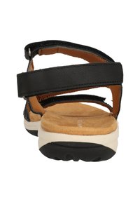 Sort sandal med to justerbare remme, en polstret suede-sål og en hvid gummisål. Har en glat læderoverflade.