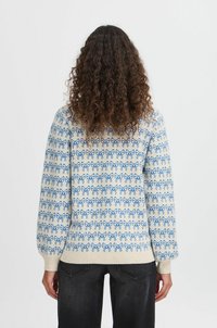 Suéter de punto con patrones de lazo azul sobre un fondo crema, con puños y dobladillo acanalados y un diseño de corte relajado.