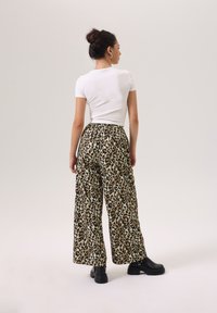 Witte top met korte mouwen, gecombineerd met wijde leopardprint broek. De broek heeft een ontspannen pasvorm en een elastische tailleband, aangevuld met zwarte laarzen.