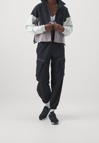 Kurtka z blokami kolorów, zapinana na zamek, w czerni, szarości i bieli; zestawiona z czarnymi spodniami typu cargo z elastycznymi mankietami i licznymi kieszeniami; czarne sneakersy.