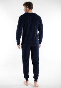 Conjunto de loungewear en azul marino que incluye una camiseta de manga larga y pantalones, con puños acanalados y una textura suave y aterciopelada.