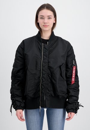 Black bomber jacket with a shiny finish, zip front, ribbed cuffs, and side pockets. Features gathered detailing and a red tag on the sleeve.