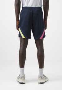 Tengerészi sportnadrág élénk rózsaszín és neon sárga átlós csíkokkal, rugalmas der�ékkal és könnyű anyagból a kényelem érdekében.