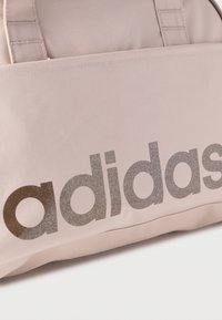 Τσάντα από ανοιχτό ροζ ύφασμα με μεγάλο, αντανακλαστικό λογότυπο "adidas" σε σκούρο γκρι. Ομαλή υφή με ενισχυμένες ραφές και ανθεκτικές λαβές.