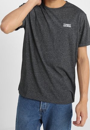 Camiseta de algodón gris oscuro con cuello redondo, mangas cortas y un logo blanco "TOMMY JEANS" en el área del pecho izquierdo.