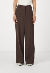 Pantalons large en marron avec une taille haute, un devant plat et des ourlets, fabriqués en tissu lisse. Associés à une chemise blanche et des talons.