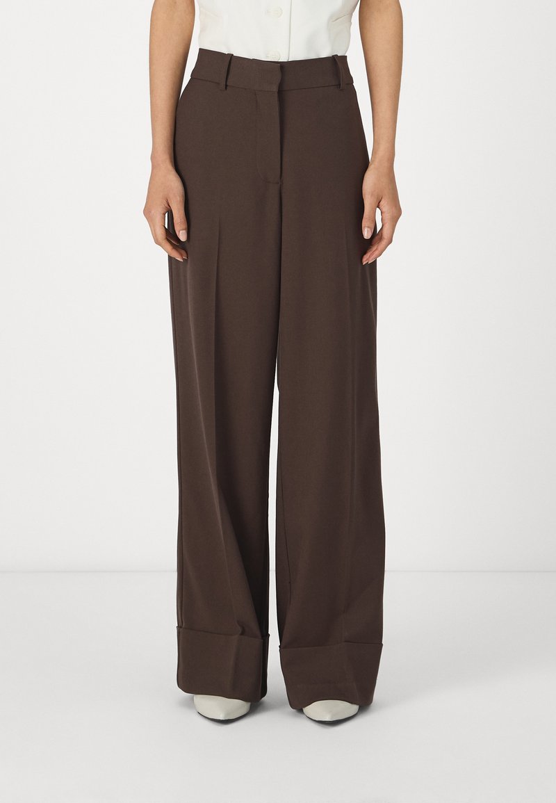 Pantalons large en marron avec une taille haute, un devant plat et des ourlets, fabriqués en tissu lisse. Associés à une chemise blanche et des talons.