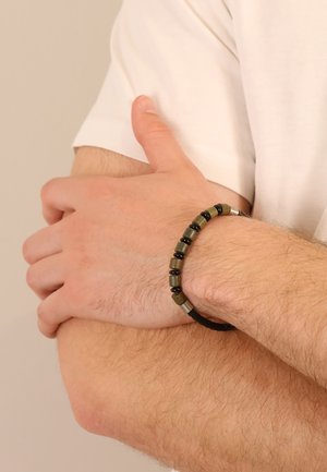 Bracelet featuring green and black beads on a woven black cord. Includes silver accents and a textured finish, shown worn on a wrist.