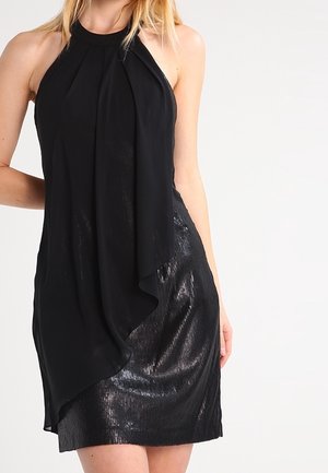 Musta halterneck-mekko, jossa on laskeutuva, drapetoitu etuosa, teksturoitu vartalo ja kiiltävä, kerroksittain laskostettu hame. Sileä kangas, jossa kevyt kiilto.