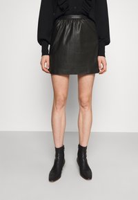 Black leather mini skirt with an elastic waistband, smooth texture, and a fitted design. Paired with black ankle boots.