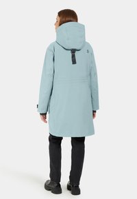 Ljusblå, vattentät parka med huva, justerbar bakrem och långa ärmar. Har en rak skärning och sidofickor.