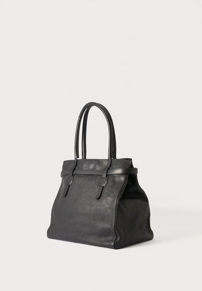 Sac à main en cuir noir avec deux longues anses et une base rectangulaire, debout sur un fond clair uni.