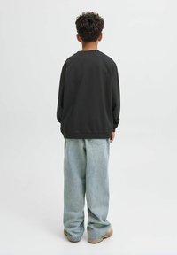 Felpa nera con fit rilassato, abbinata a jeans baggy azzurri chiari e scarpe beige, vista da dietro su uno sfondo semplice.