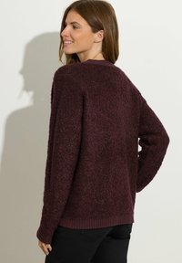 Bordowy sweter o teksturowanej powierzchni, z luźnym krojem, ściągaczami na rękawach i u dołu. Miękki materiał, okrągły dekolt, widoczne szwy.