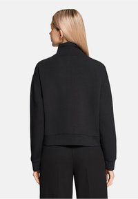 Czarna krótka bluza z wysokim kołnierzem i długimi rękawami. Miękka tkanina o gładkiej fakturze i ściągaczowe mankiety. Minimalistyczny design.