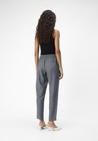 Pantaloni grigi a sigaretta in tessuto texturizzato con vita elastica, dotati di tasche laterali e bordo rifinito, abbinati a un top senza maniche nero.