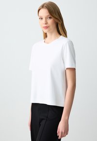 Witte katoenen t-shirt met een ronde hals en korte mouwen, met een losse pasvorm en een gladde textuur. Gecombineerd met zwarte broek.