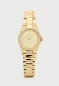 Zelta krāsas rokas pulkstenis ar astoņstūra seju, minimālistisku ciparnīcu un strukturētām detaļām. Pārī savienojamo saišu dizains drošai piestiprināšanai. Zīmola nosaukums redzams.