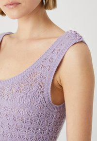 Top lavorato a maglia lilla con un motivo testurizzato, spalline ampie e dettagli con bottoni sulla spalla. Materiale morbido con un design leggero.