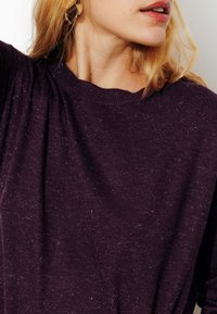 Pull violet en tissu texturé, avec un col rond et une coupe douce et décontractée. De fines speckles ajoutent des détails à la surface du tissu.