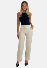 Zwarte mouwloze bodysuit gecombineerd met hoog-gesneden beige broek met knoopsluiting en zijzakken. Gladde stof, getailleerde pasvorm.