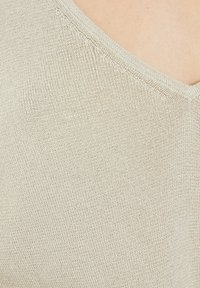Vaahto beige v-paita, jossa on teksturoitu neulekangas. Korostaa hienovaraisia ompeleita kaula-aukossa ja pehmeää, kevyttä muotoilua.
