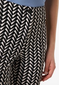 Schwarz-weiße Hosen mit Zickzackmuster aus glattem Stoff, mit einem schwarzen Knopfverschluss und einem gerippten blauen Bund.