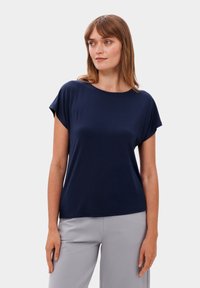 Námořnická modrá tričko s krátkým rukávem a kulatým výstřihem, vyrobené z měkké látky. Mírně volný střih, zkombinované se světle šedými sakovými kalhotami.