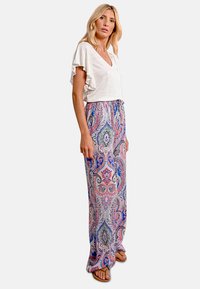 Lunga gonna a fantasia paisley in blu, rosa e verde, abbinata a una blusa bianca a maniche corte con volant. Stile casual, tessuto morbido e vestibilità ampia.