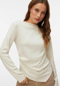 Lang shirt met lange mouwen in crèmekleur, met een boothals. Gladde textuur, aansluitende pasvorm en subtiel geplooid detail bij de zoom.