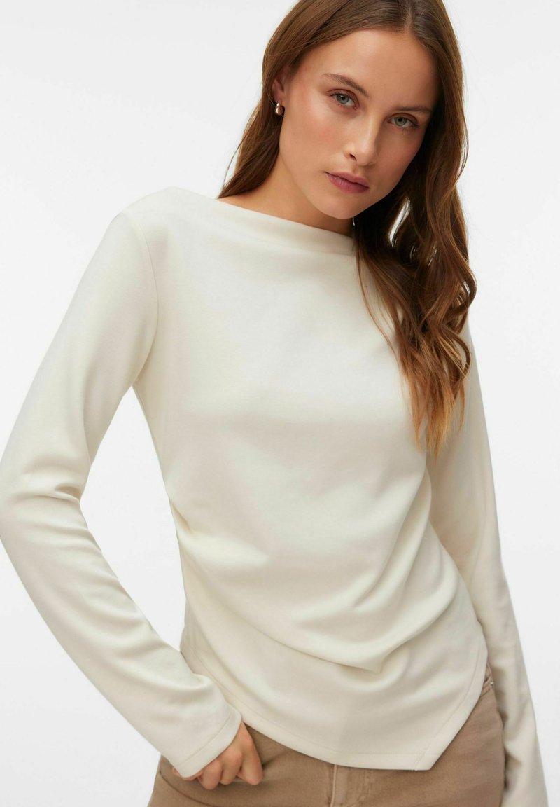 Lang shirt met lange mouwen in crèmekleur, met een boothals. Gladde textuur, aansluitende pasvorm en subtiel geplooid detail bij de zoom.