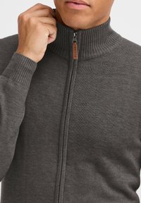 Dunkelgrauer Reißverschluss-Pullover mit geripptem Kragen und Bündchen. Verfügt über eine glatte Textur und ein Lederetikett am Reißverschluss. Figurbetontes Design.