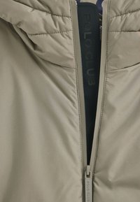 Giacca puffer beige con chiusura a zip caratterizzata da una texture morbida e liscia. L'etichetta interna riporta la dicitura "POLO CLUB." Design con cappuccio e dettagli cuciti.