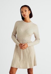 Robe en tricot côtelé beige avec des manches longues, un col rond et un corsage ajusté qui s'évase à la taille. Texture douce, silhouette décontractée.
