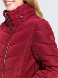Rote Steppjacke mit hohem Kragen, Reißverschluss und gemusterten Seitenpaneelen. Verfügt über eine glänzende Textur und silberne Applikationen.