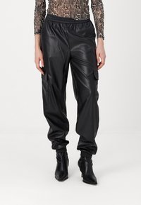 Zwarte neplederen cargobroek met een elastische tailleband, voorzien van zijzakken en boorden, gecombineerd met zwarte enkellaarzen.
