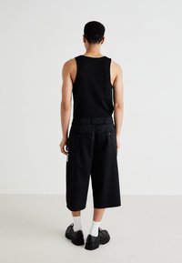 Top negru fără mâneci asortat cu șorturi negre, cu picioare lejere. Detalii notabile includ două buzunare la spate și pantofi negri cu tinte distinctive.