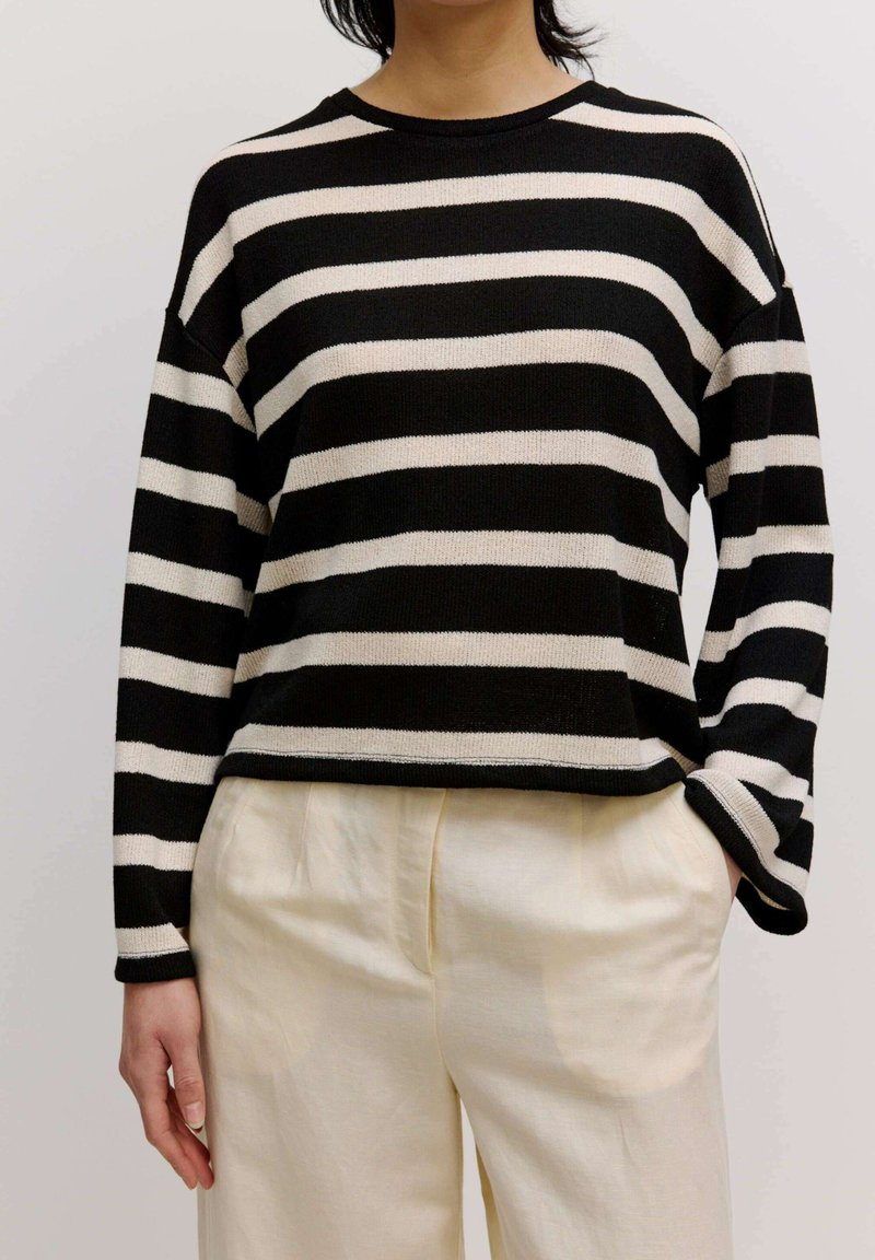 Zwart-wit gestreepte trui met een ontspannen pasvorm, geribbelde halslijn en een drop shoulder ontwerp, gecombineerd met lichtcrèmekleurige, wijde broek.