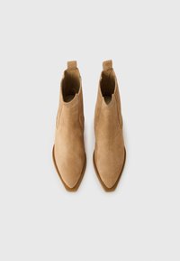 Botine din pielă-suede, de culoare tan, cu vârf ascuțit, panouri elastice pe laterale și bucle la partea de sus pentru o îmbrăcare ușoară. Textură netedă.