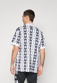 Camisa de manga corta con un patrón geométrico en blanco y negro, que presenta un cuello acanalado y un acento rosa, hecha de un tejido ligero.
