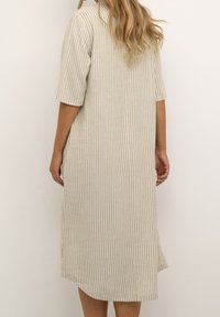 Vestido beige claro con rayas verticales blancas, mangas cortas, aberturas laterales y un corte holgado, hecho de una tela texturizada.