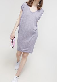 Abito corto a maniche corte in lavanda, dal taglio morbido e con scollatura a V, realizzato in tessuto morbido. Abbinato a sneakers bianche e con una pochette colorata.