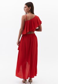 Completo rosso a due pezzi composto da un top monospalla con dettagli arricciati e una lunga gonna maxi fluida. Realizzato in un tessuto leggero e texturizzato.