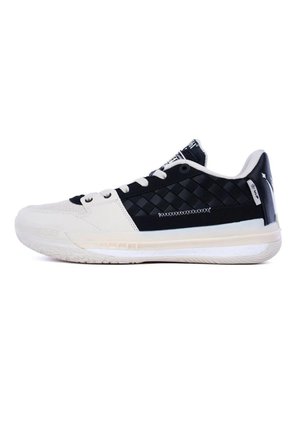 Zapatilla deportiva de corte bajo con bloques de color negro y blanco, cordones blancos, un patrón tejido en el lateral y una suela gruesa acolchada.