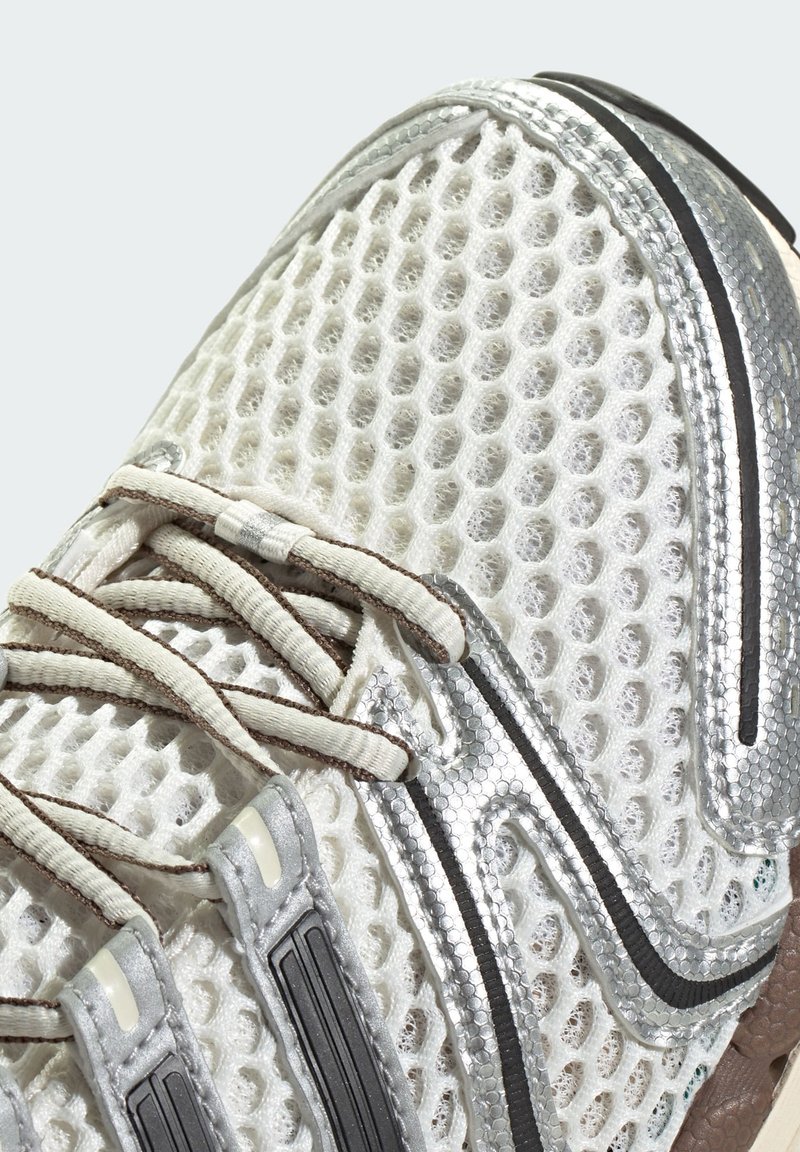 Weißer Netz-Sportschuh mit silbernen Akzenten und beigen Schnürsenkeln, der die detaillierte Textur und den vorderen oberen Abschnitt zeigt.