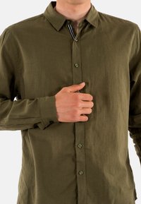 Olijfgroen overhemd met knopen, gemaakt van getextileerd materiaal; heeft een klassieke kraag, lange mouwen en een subtiele streepdetail aan de binnenkant van de kraag.