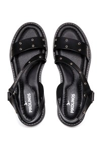 Sandales noires en cuir avec plusieurs brides horizontales ornées de clous métalliques et une semelle intérieure texturée. Bride de cheville ajustable avec fermeture à boucle.