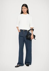 Hvit kortermet topp med teksturert finish, kombinert med høytlivede mørkeblå vidbenede jeans og en liten svart veske med nagler.